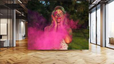 Pleased caucasian woman iwith curly hair standing n a cloud of pink dry paint, celebrating Holi festival Wall mural