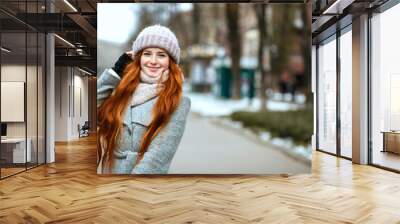 Urban portrait of happy redhead woman with long hair wearing warm clothes walking at the city. Empty space Wall mural