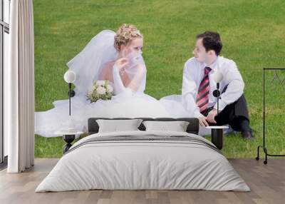 bride and groom sit on the grass and look to the eyes Wall mural