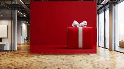 A beautifully wrapped red gift box with a white ribbon sits on a plain red background symbolizing joy, celebration, and surprises, perfect for any festive occasion. Wall mural