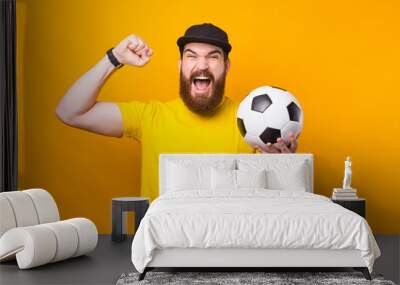 Amazed bearded hipster man celebrating victory and holding soccer ball Wall mural