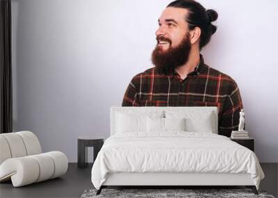 Cool man with beard using phone and looking up. Casual young man using  smartphone and smiling on white background with copy space. Wall mural