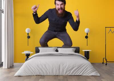 Full length portrait of excited bearded man jumping and showing thumbs up isolated over yellow background Wall mural