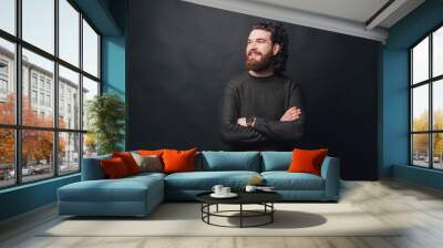 Handsome man with beard and long curly hair standing over dark background with crossed arms and looking away. Wall mural