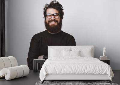 Happy smart handsome young man wearing glasses and smiling at camera crossing arms on white background. Wall mural