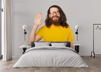 Hey Hello Welcome, Cheerful bearded man with long hair smiling and making saluting gesture. Wall mural