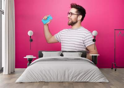 Photo of a handsome man listening music with aipods and dancing over pink background Wall mural