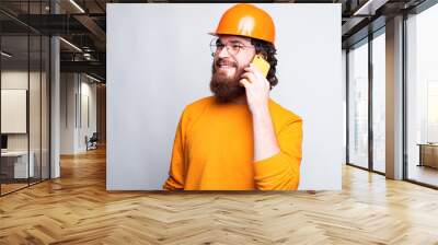 Photo of bearded young architect wearing helmet and talking on phone. Wall mural