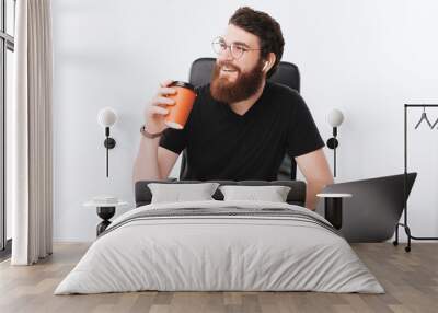 Photo of young bearded freelancer, thinking at something while drinking coffee, isolated background Wall mural