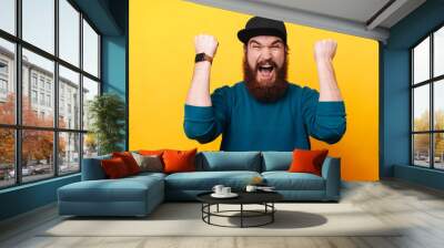 Portrait of amazed bearded man celebrating success over yellow background Wall mural