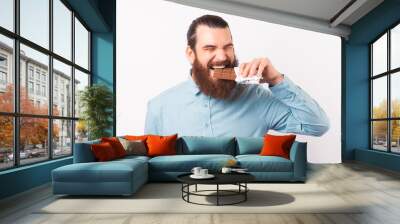 Portrait of bearded man in casual eating bar of chocolate over white background Wall mural