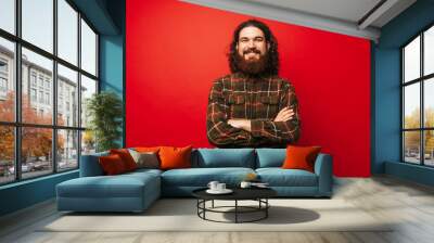 Portrait of cheerful bearded hipster man with crossed arms over red background Wall mural