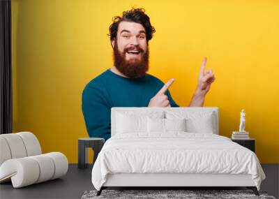 Portrait of cheerful bearded man pointing away over yellow background Wall mural