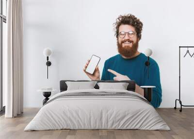 Portrait of happy bearded man pointing at blank screen on smartphone Wall mural