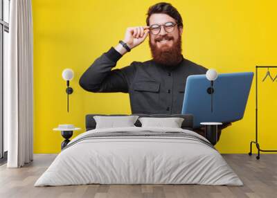 Portrait of happy smart bearded guy, holding a laptopand touchig his glasses Wall mural