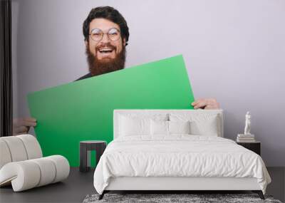 Portrait of smiling bearded man holding blank banner in hands isolated on gray background Wall mural