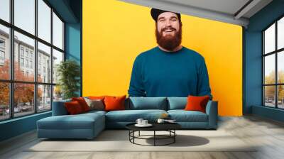 Portrait of young hipster man in hat posing on yellow background. Smiling bearded man wearing sunglasses, studio shot. Wall mural