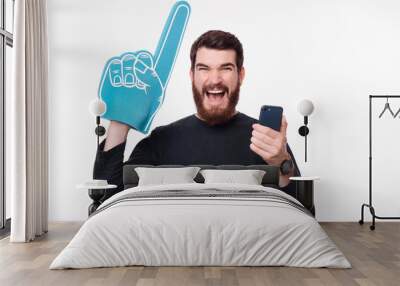 Screaming bearded man is holding his phone and fan foam finger glove Wall mural