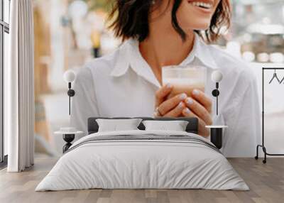 Wonderful smiling woman holding a glass of latte is walking on the street on a sunny day. Wall mural