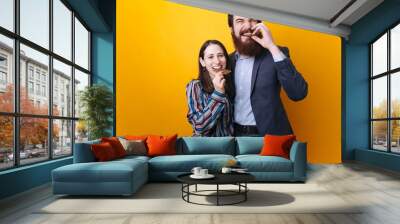 Young couple man and woman eating chocolate on isolated yellow background Wall mural