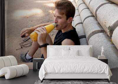 young man sitting on the floor and leaning against the wall drinking water Wall mural