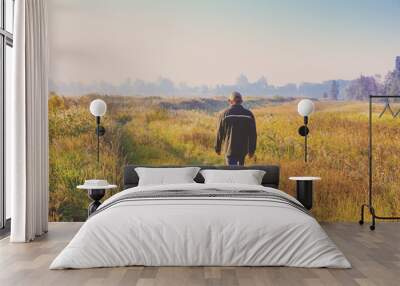 A man walking along a country road through the field early in the morning Wall mural