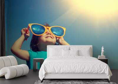 Happy little girl with big sunglasses looking at the sun Wall mural