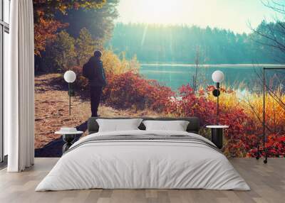 Man tourist stands on a picturesque lakeshore in the autumn morning and looking at the sunrise Wall mural