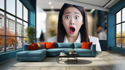 Amazed Asian businesswoman reacts to camera says wow in office Shocked female student celebrates good news indoors copy space image Wall mural