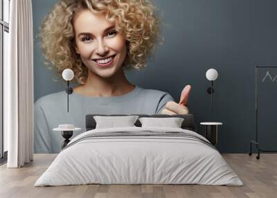 Blonde woman smiling pointing with thumb up against grunge grey background Wall mural