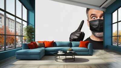 Concept of coronavirus lifestyle and quarantine Portrait of a surprised attractive middle aged man looking and pointing to the right dressed in a black medical mask and gloves set against a white bac Wall mural