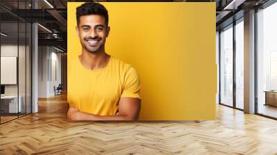 Confident Indian man in casual t shirt stands with arms crossed on yellow background representing success Wall mural