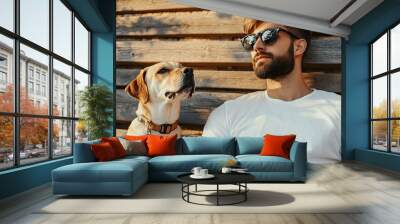 Low angle shot of a young handsome male with a beard dressed in a white t shirt and eyeglasses relaxing on a wooden bench with a purebred dog on a leash gazing off to the side. with copy space image Wall mural