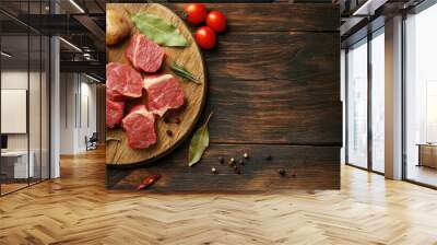 Raw meat two types of spiced pickled meat medallions on a circular wooden board on the table accompanied by garlic bay leaves potatoes and tomatoes cooking idea copyspace Wall mural