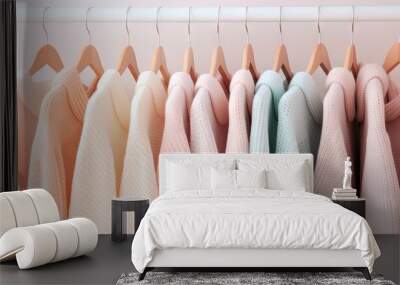 Sweaters in pastel colors hang on white hangers Wall mural