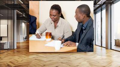 Young woman smiling takes notes at a business meeting while two men at her side looks at her writing Wall mural