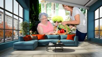 cheerful mature woman delivering an organic vegetable basket at home to an elderly senior woman Wall mural