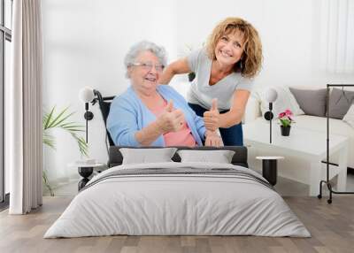 cheerful mature woman visiting retirement home residence with elderly senior woman on wheelchair Wall mural