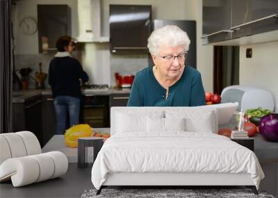 happy senior active woman cooking at home in modern kitchen and looking for recipe on a internet computer tablet Wall mural