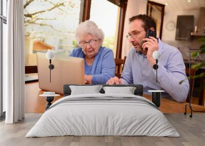 mature man helping elderly senior woman at home with paperwork and computer internet lesson Wall mural