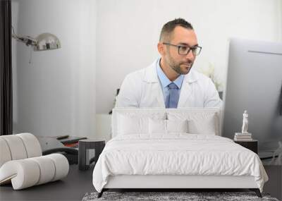 portrait of a handsome man male doctor in medical practice office working on computer Wall mural