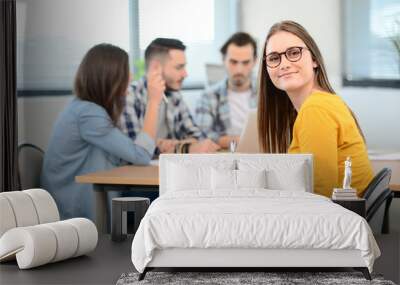 portrait of young woman in casual wear working in a creative business startup company office with coworker people in background Wall mural