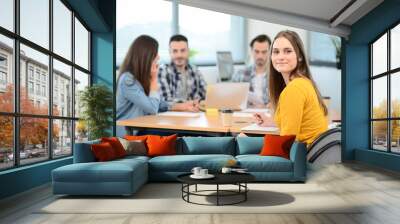 portrait of young woman in casual wear working in a creative business startup company office with coworker people in background Wall mural