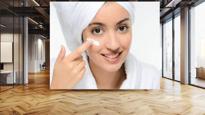 young ethnic woman in white peignoir putting on skincare facial cream Wall mural