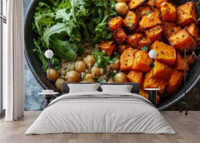 A vibrant shot of a vegan Buddha bowl filled with quinoa, chickpeas, roasted sweet potatoes, and leafy greens. Wall mural