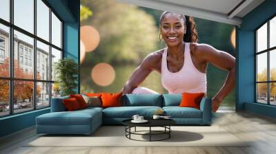 Bellissima donna di origini africane con abbigliamento sportivo rosa per il fitness sorride mentre fa jogging in mezzo ad un parco nella natura Wall mural