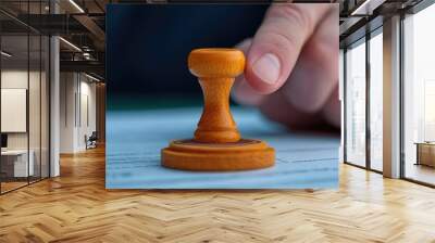 A close-up of a hand pressing a wooden stamp on a document, symbolizing approval or certification in a professional setting. Wall mural