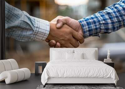 Close-up of a firm handshake between two people wearing checkered shirts, symbolizing agreement and partnership in a professional setting. Wall mural