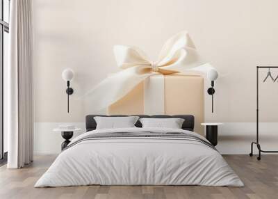  A beige gift box, adorned with a white ribbon and a bow atop, sits serenely on a pristine white surface Wall mural