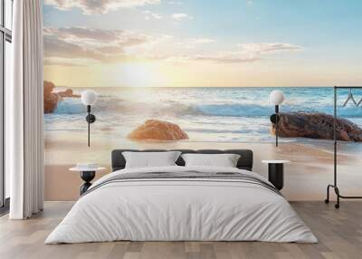  A couple of rocks atop a sandy beach, adjacent to a tranquil body of water and a radiant sun in the backdrop Wall mural